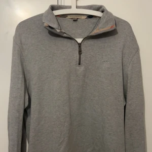 Grå långärmad tröja med dragkedja från Burberry - Säljer en stilren grå långärmad tröja från Burberry med halv dragkedja framtill och klassisk krage. Perfekt för lager-på-lager och har diskret logga på bröstet. Skön och mjuk bomullskvalitet. Köptes i london går ej o köpa längre, Pris 500 kr