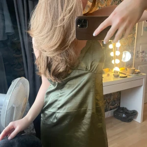 Grön satinklänning med spetsdetaljer - Säljer en grön satinklänning med smala axelband och v-ringning. Klänningen har fina spetsdetaljer längs urringningen och är i ett glansigt, mjukt material. Aldrig använd, lappen kvar!!💚