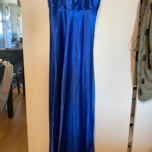 Blå långklänning i satin - Säljer en elegant blå långklänning i glansigt satinmaterial. Klänningen har en figurnära passform upptill och faller snyggt längs kroppen. Perfekt för bal eller festliga tillfällen. Axelbandslös design som ger en stilren look.