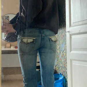Blå jeans med dekorerade bakfickor - Säljer ett par blå jeans med snygga detaljerade bakfickor och låg midja. Jeansen är raka i passformen!  Fickorna har dekorativa detaljer som ger byxorna en unik look. Står strl S på lapp men passar som en xs! 79cm innerben, 36cm midja!