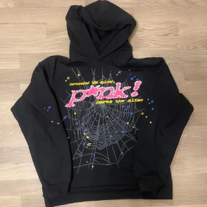 Svart hoodie med spindelnätsmönster och tryck - Cool svart hoodie med stort spindelnätsmönster och färgglatt tryck på bröstet. Texten är i rosa och gult med små stjärnor i blått och gult runtom. Perfekt för dig som gillar streetwear och unika plagg. Storlek M men passar S
