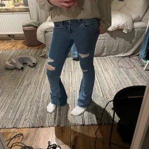 Blå bootcut jeans med slitningar - Säljer ett par blå bootcut jeans med slitningar på båda benen. Jeansen har normal passform och är i klassisk denim med snygga detaljer vid knäna. Perfekta för en avslappnad och trendig look. Sytt om jeansen för att göra de mer utsvängda, Jeansen är lite söndertrampade bak men inget man tänker på😇