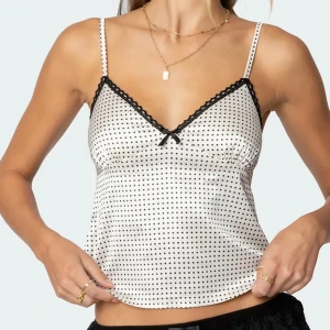 Vit prickig linnetopp med spetsdetaljer - Helt ny! Söt vit linnetopp med små svarta prickar och tunna axelband. Toppen har svart spetskant och en liten rosett framtill. Från Edikted💖köptes nyligen för ca 450kr då frakt kostar runt 120. Vill ej skicka tillbaka helst, lappar osv är kvar! 