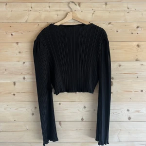 Svart festtopp  - Svart glansig topp perfekt för festliga tillfällen. Lätt halterneck. Bra kvalité med ett lite tjockare veckat tyg (se bild 5). Perfekt passform som framhäver  en väld fin timglasfigur. Strl M från NA-KD. Cropped vid typ naveln på mig som är 174 cm. 