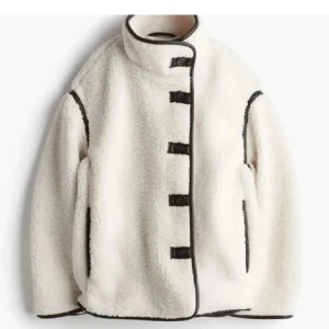Hm teddyjacka - Säljer en mysig vit teddyjacka med svarta kantdetaljer och unika knäppningar framtill. Jackan har en hög krage och långärmade ärmar, perfekt för kyliga dagar. En stilren och trendig jacka för alla tillfällen. KAN GÅ NER I PRIS VID KÖP UTANFÖR APPEN