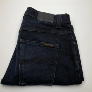 Svarta jeans Nudie Jeans Grim Tim - Snygga svarta jeans från Nudie Jeans, modellen Grim Tim. Jeansen har klassisk femficksdesign, svarta sömmar och är tillverkade i ekologisk bomull med lite stretch för extra komfort. Perfekta för dig som gillar en stilren look. 32/34 uppsydda så passar 32/32