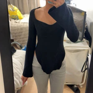 Svart ribbad långärmad topp - Säljer en svart ribbad topp med lång ärm och snygg v-ringad halsringning. Toppen har en figurnära passform och är tillverkad i ett stretchigt material som sitter skönt på kroppen. Perfekt att styla med jeans eller kjol.