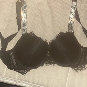 Svart spets bh Victoria's Secret - Supersnygg svart korsettopp från Victoria's Secret med spetsdetaljer och glittriga axelband. Kuporna är vadderade och har en lyxig känsla med spets runt kanterna. Perfekt för att lyfta vilken outfit som helst.