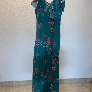 Blommig långklänning från Rut&Circle - Säljer en snygg långklänning från Rut&Circle i storlek S. Klänningen är grön med rosa och röda blommor, har v-ringning och volangdetaljer vid axlarna. Materialet känns lätt och luftigt, perfekt för sommarens alla tillfällen. Supersöt och trendig look!