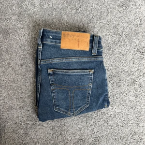 Blå skinny jeans Slight 29/30 - Snygga blå skinny jeans från tiger of Sweden med modellen Slight i klassisk tvätt med diskreta slitningar. Modellen har fem fickor, gylf med dragkedja och smal passform hela vägen ner. Perfekta för dig som gillar en tajt look och vill ha ett par stilrena jeans till vardags.