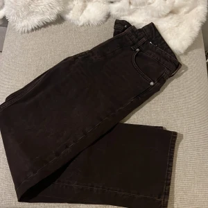 Bruna straight jeans från H&M &Denim - Mörkbruna jeans från H&M &Denim i rak modell med relaxed straight fit och midwaist. Klassisk femficksdesign, silverfärgade nitar och läderpatch bak. Snygga till sneakers eller boots, tillverkade i bomull för en skön känsla.