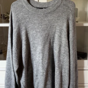 Grå stickad tröja med rund hals - Mysig grå stickad tröja med rund halsringning och långa ärmar. Perfekt för lager-på-lager och chill dagar. Enkel och stilren design som funkar till det mesta. Oversized fit för extra comfort.