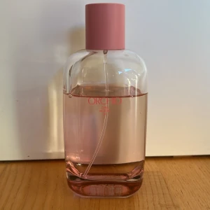 Zara Orchid parfym rosa flaska - Fräsch parfym från Zara i doften Orchid. Flaskan är genomskinlig med ljusrosa vätska och har ett stilrent, rundat utseende. Locket är matt rosa och flaskan är gjord av glas. Perfekt för dig som gillar blommiga och feminina dofter.