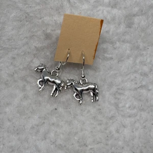Silvriga örhängen med hästmotiv - Ett par coola silvriga örhängen med detaljerade hästberlocker. Perfekta för dig som älskar hästar och vill ha något unikt i din stil. Hängande modell som ger en snygg touch till din outfit.krokarna är i sterling silver 