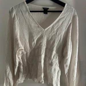 Vit blus med v-ringning från Lindex - Säljer en vit blus från Lindex med v-ringning och lång ärm. Blusen har en lätt skrynklig struktur och är tillverkad i ett tunt, luftigt material. Perfekt för dig som gillar en avslappnad men ändå stilren look.