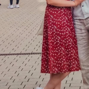 Röd blommig kortklänning med volangärm - Superfin röd kortklänning med små vita blommor och volangärmar. Klänningen har v-ringning och knappar framtill, vilket ger en söt och somrig look. Perfekt för dig som gillar romantiska detaljer och vill ha en luftig klänning till varma dagar.