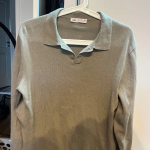 Grön pikétröja från Zara - Snygg grön pikétröja från Zara med klassisk krage och två knappar framtill. Tröjan är långärmad och tillverkad i ett mjukt material som passar perfekt till skolan eller häng med kompisar.