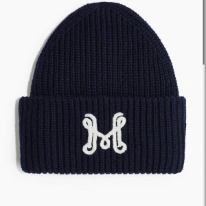 Mörkblå ribbstickad mössa med M-brodyr - Snygg mörkblå ribbstickad mössa med vit broderad M på uppvikt kant. Perfekt för kalla dagar och ger en cool touch till din outfit. Tjockt stickat material som håller dig varm och stilen på topp. Så