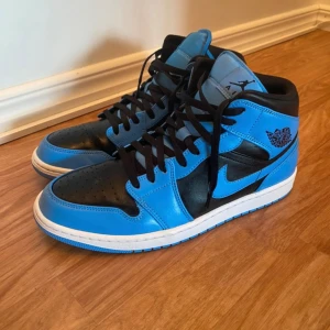 Nike Air Jordan 1 High blå/svarta - Säljer ett par Nike Air Jordan 1 High i blått och svart skinn med vita sulor. Klassisk siluett med svart snörning, rund tå och ikoniska Jordan-loggor på sidan och tungan. Perfekta för dig som vill sticka ut med stilrena sneakers.