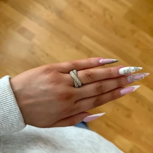 Guldring med stenar från Pilgrim - Säljer en supersnygg guldfärgad justerbar ring med stenar och korsad design från Pilgrim. Den är använd och har några defekter (se bilder), saknar bl.a. en sten. Men tänker att det kanske är någon som vill ha den ändå eftersom denna modell inte säljs längre i guld. Nypris 449kr