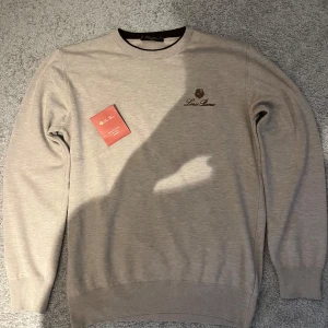 Loro Piana tröja - Snygg beige tröja från Loro Piana med brunt broderat logotyptryck på bröstet. Perfekt för dig som gillar stilrena och exklusiva plagg. Tröjan är oanvänd då den inte passade mig. Tröjan är storlek L men passar M