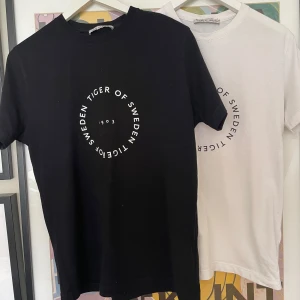 Tiger of Sweden t-shirt svart & vit - Två stilrena t-shirts från Tiger of Sweden i svart och vitt med cirkelformad logga framtill. Klassisk passform. Vita tröja har en söms som är lite lös, se bild 2. Storlek M men skulle säga mer en passform som S, kom privat för fler funderingar och frågor. 1 för 150 2 för 300 Priset är ej hugget i sten.