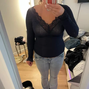 Mörkblå långärmad tröja  - Säljer en mörkblå långärmad blus med v-ringning och fina spetsdetaljer vid halsringning och ärmslut. Toppens material är tunt och lätt genomskinligt. Den har små håll som är igensydda vid slutet på magen. Säljer då jag inte har användning av den längre.