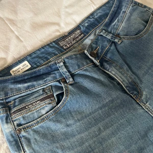 Blå bootcut jeans från Diesel - Säljer ett par blå low waist, vintage bootcut jeans från Diesel i väldigt bra skick och snygga slitningar. Jeansen har flared ben och slim fit över låren. Materialet är 98% bomull och 2% elastan för lite stretch. Perfekta för dig som gillar en avslappnad men ändå trendig look, då de är väldigt bekväma men sitter väldigt fint. Storlek 30 i midjan och 32 i benen. M/L