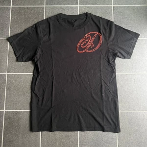 2kdeema tshirt - Svart t-shirt i bomull med en stor röd broderad logga på bröstet. Klassisk rund halsringning och korta ärmar. Perfekt för en chill och stilren look.