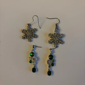 Två par glittriga örhängen - Säljer två par örhängen: ett par i form av snöflingor med gnistrande stenar och ett par med gröna och klara stenar i olika storlekar. Båda paren är i silverfärg och perfekta för att ge din look extra bling. Mycket fint skick! Knappt använda.