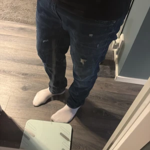 Mörkblå slitna jeans från Dondup - Säljer ett par mörkblå jeans från Dondup med snygga slitningar och distressed detaljer. Jeansen har klassisk femficksdesign, raka ben och är tillverkade i mjukt denimtyg. Perfekta för dig som gillar en avslappnad och trendig look. Jeansen är i storlek 32/32 och i otroligt bra skick