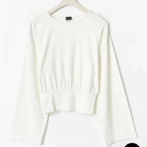 Vit långärmad tröja från Gina Tricot - Vit långärmad tröja från Gina Tricot med bred resår i midjan som ger en snygg siluett. Tröjan har rund halsringning och vida ärmar för en trendig look. Perfekt att styla med jeans eller kjol för en clean och fräsch outfit.