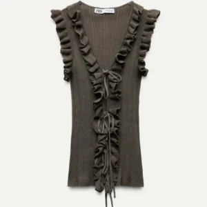 Olivgrön ribbad volangtop från Zara - Supersnygg olivgrön ribbad topp från Zara med volangdetaljer längs axlar och halsringning. Toppen är ärmlös och har v-ringad front med snörning. Perfekt för dig som gillar romantiska vibes och vill sticka ut med coola detaljer.