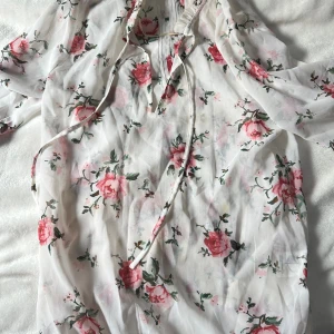 Vit blommig blus  -  vit blus med rosa blommigt mönster och gröna blad. 