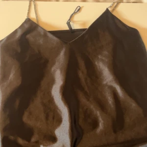 Svart satin klänning med strassband - Supersnygg svart klänning från ONLY i satin med glittrande strassband som axelband. V-ringad och figurnära passform, perfekt för dig som vill sticka ut. Stilren och elegant look med lyxig känsla. Passar dig som gillar att glänsa och vill ha något extra.