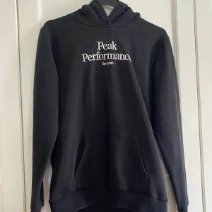 Svart hoodie från Peak Performance - Svart hoodie från Peak Performance med broderad vit logga på bröstet. Perfekt för chill dagar eller när du vill ha en clean och enkel stil. Den är storlek 170 men passar även XS. Skriv om du har frågor.