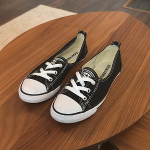 Svarta Converse sneakers låga - Klassiska svarta Converse sneakers med vit tå och vita snören. Låg modell med tydliga vita sömmar och platt sula. Perfekta till jeans eller shorts för en avslappnad stil. Ikonisk logga på plösen och insidan. Skorna är i tyg och har rund tå.