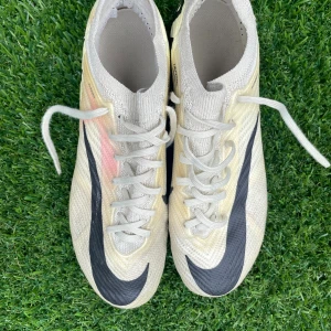 Nike Mercurial Zoom fotbollsskor beige - Säljer ett par Nike Mercurial Zoom vapor elite. fotbollsskor i beige med svarta detaljer och stora svarta swoosh-loggor. Skorna har snörning, platt sula med dobbar och är tillverkade i ett lätt syntetmaterial med Flyknit-teknologi. Perfekta för dig som vill ha grymt grepp på planen.