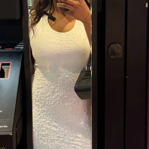 Vit halterneck kortklänning - Supersnygg vit midi klänning med strukturerat tyg och ärmlös design. Klänningen har en rund halsringning och sitter figurnära för en clean och fräsch look. Perfekt för dig som gillar stilrena och enkla outfits.