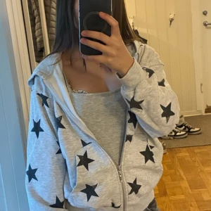 Grå hoodie med svarta stjärnor Lindex - Grå hoodie från Lindex med svarta stjärnor över hela tröjan. Dragkedja framtill, huva och känguruficka. Perfekt för dig som gillar en chill och snygg stil. Mjuk bomullskänsla och långärmad modell!🩷💕💕