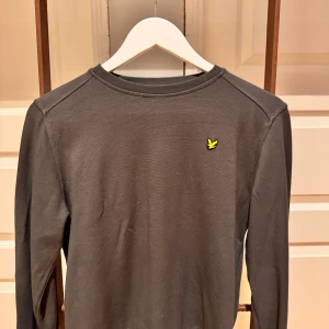 Mörkgrön långärmad tröja Lyle & Scott - Snygg mörkgrön långärmad tröja från Lyle & Scott med klassisk rund hals och den ikoniska gula fågel-loggan på bröstet. Perfekt basic-plagg som funkar till allt. Mjuk bomullskvalitet som är skön att ha på sig hela dagen.
