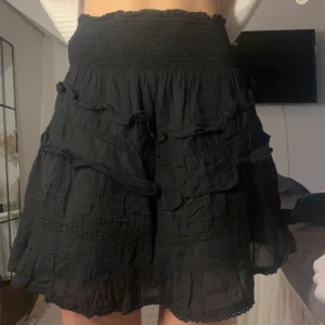 Svart volangkjol från Neo Noir - Supersöt svart kortkjol från Neo Noir med flera volang detaljer. Kjolen har en luftig känsla och är perfekt till sommaren eller fest! Den går att vika ner om man vill det 💕