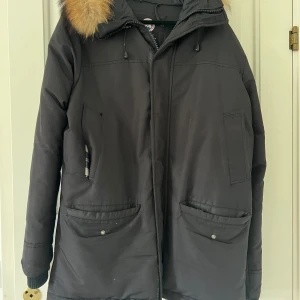 Svart parkas från Canada Goose - Säljer en svart parkas från Canada Goose med stor huva och äkta pälsdetalj. Jackan har flera fickor framtill, ribbade muddar och klassisk logga på ärmen. Perfekt för kalla vinterdagar och riktigt snygg till streetwear-stilen.