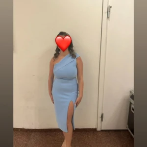 Ljusblå oneshoulder klänning med slits - Säljer en ljusblå, figurnära klänning med oneshoulder-design och snygg slits framtill. Klänningen har en stilren look och är perfekt för dig som vill sticka ut. Materialet känns mjukt och följsamt mot kroppen. Passar dig som gillar trendiga och eleganta plagg.