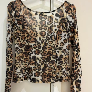 Ny Leopardmönstrad mesh topp - Snygg långärmad topp i mesh med leopardmönster i bruna, svarta och beige toner. Toppen har rundad urringning och figurnära passform, perfekt för att sticka ut. Tunn och lätt, passar till många olika stilar.