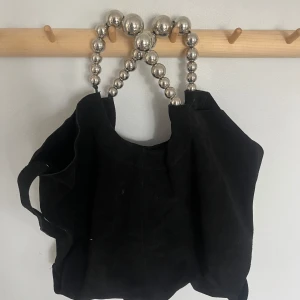 Svart mocka axelväska från Zara - Cool svart axelväska från Zara i mocka med unika handtag av stora silvriga kulor. Väskan har även en lång axelrem och stängs med magnetknapp. Använd fåtal gånger och är fortfarande i bra skick utan deffekter. 