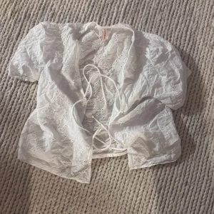 Vit broderad bolerotopp med knyt - Söt vit bolerotopp från only med broderade detaljer och knyt framtill. Tunn och luftig med korta ärmar, perfekt för lager-på-lager och sommarvibbar. Ger en romantisk och trendig look.
