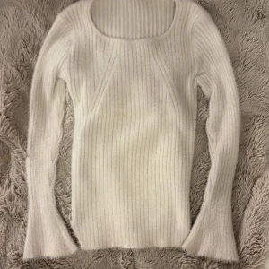 Vit ribbad stickad tröja med utsvängda ärmar - Supermjuk och fluffig vit stickad tröja med ribbat mönster. Tröjan har långärmade, lätt utsvängda ärmar och en kroppsnära passform. Perfekt för lager-på-lager och ger en clean, stilren look. Materialet känns lyxigt och värmande.