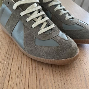 Grå sneakers från Maison Margiela - .Tjena, säljer nu dessa maison margiela gats i storlek 40. Det är i utmärkt skick original box tillkommer och kvitto kan skickas. Hör av er för fler bilder eller funderingar priset går att diskutera!!