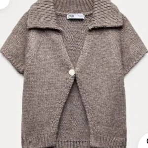 Beige/brun stickad kofta från Zara - Säljer min beige/bruna stickad kofta från Zara med korta ärmar, bred krage och en stor knapp framtill. Koftan har ribbade detaljer vid krage, ärmslut och nederkant. Perfekt att slänga över en t-shirt för en chill look.